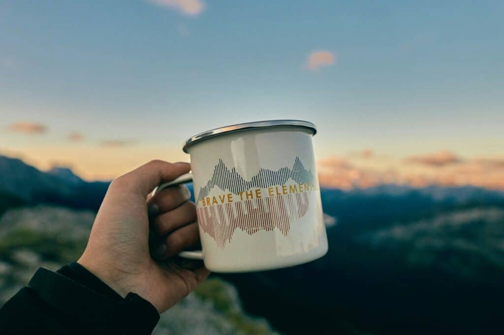 An enamel mug held up outdoors at dusk