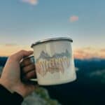 An enamel mug held up outdoors at dusk